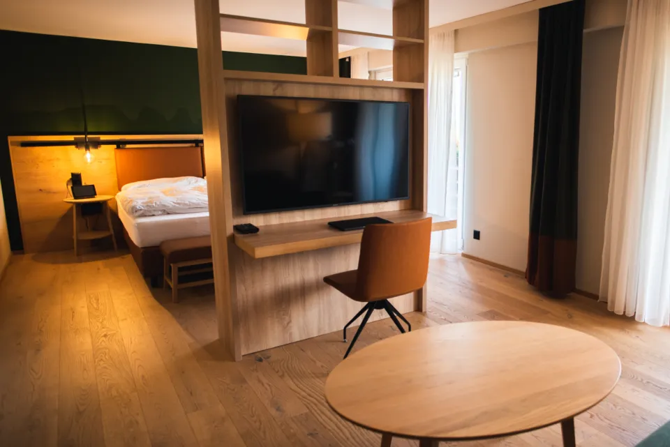 A modern hotel room with a wooden desk partition, bed and round table